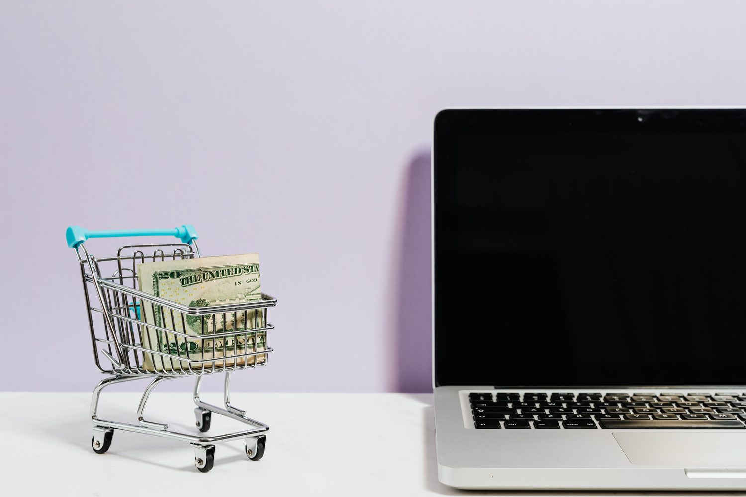 A miniature shopping cart beside a laptop representing ecommerce